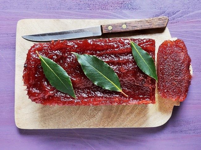 Plum_membrillo_garnished_with_fresh_bay_leaves_being_sliced