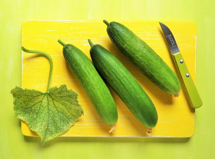 3_mini_cucumbers_with_leaf_on_yellow_chopping_board